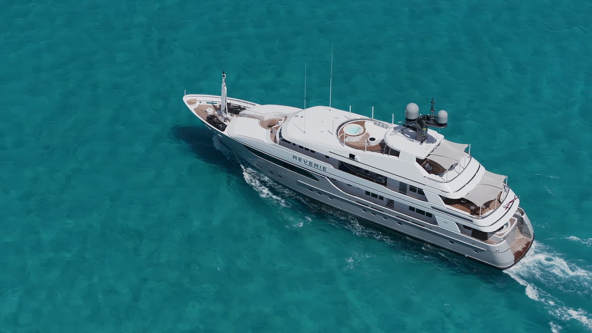 Aerial view of a white superyacht cruising across turquoise water